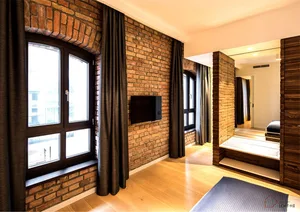 A modern living room featuring a brick wall, hardwood flooring, and a large arched window.