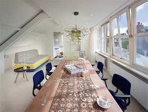 A modern living room with a wooden table covered in puzzle pieces and a blue chair.