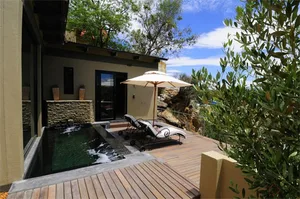 A modern outdoor deck featuring a swimming pool, lounge chairs, and a large umbrella. Surrounded by natural elements and ston