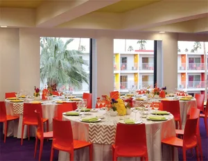 A lively, modern hotel ballroom with red chairs and white tablecloths