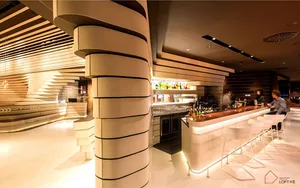 A modern restaurant bar with illuminated wood and metal accents, glass shelves, and seating area.