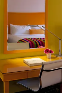 A modern bedroom with yellow furniture, a colorful striped blanket, and a white chair.