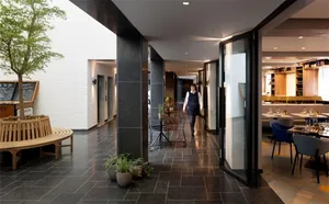 A modern restaurant corridor featuring concrete columns, granite flooring, and indoor plants.