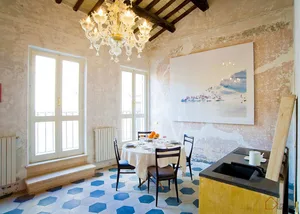 A cozy dining room with a round table, white chairs, and blue hexagonal tiles on the floor. The ceiling features exposed wood