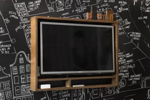 A wall-mounted electronics shelf with a wooden frame and a black flat-screen TV on it, against a chalkboard wall.