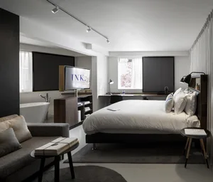 A modern minimalist hotel room with a bed, sofa, bathtub, and television.