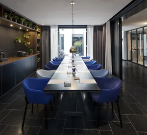 Modern conference room with long table, blue chairs, and green plants.