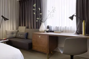Modern, minimalist home office with a wooden desk, white vase with greenery, and black desk lamp.