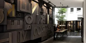 An interior lobby with a modern, metal typography wall and a wooden table with two people.