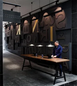 Man standing at a long wooden reception desk in a modern office interior, with a wall of large, 3D-rendered letters in dark t