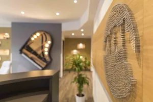 Modern reception desk made of wood with a plant in the background and a piano-shaped mirror on the wall.