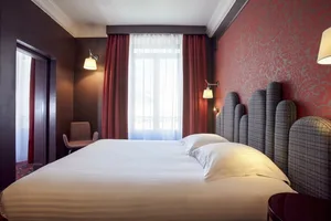 A neatly made bed with white linens and red, patterned curtains in a hotel bedroom setting.
