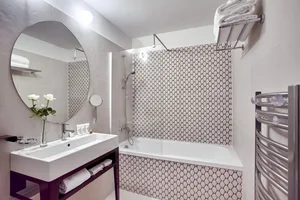 Modern minimalist bathroom with patterned ceramic tiles, featuring a walk-in shower, white vanity with sink, and a towel rack