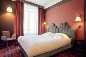 A minimalist bedroom with a white bed, red curtains, and a red patterned wall.