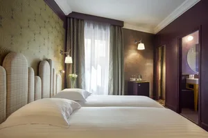A modern bedroom featuring a twin bed with white bedding, white headboard, and a window with curtains and a vase of flowers.