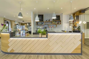 Modern coffee shop with a counter made of wood and aluminum, featuring a wooden floor and white pendant lights.