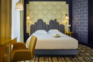 Modern hotel bedroom with white sheets, grey headboard, and mustard chair.