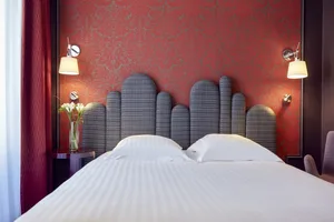 A modern hotel bedroom with a bed, headboard, and red wallpaper.