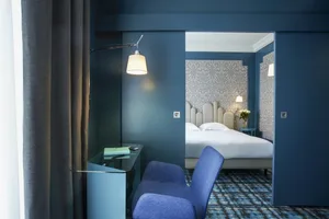 A modern hotel room with blue walls, fabric headboard, and glass desk.