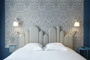 Modern hotel room featuring a textured wallpaper and upholstered bed with white pillows and lamps.