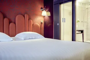 Modern minimalist bedroom with a white bed, orange upholstered headboard, and glass doors to the bathroom.