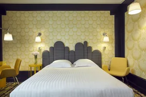 Modern bedroom featuring a double bed adorned with white bedding against a bold yellow patterned wallpaper backdrop.