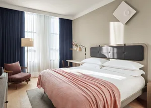 A minimalist bedroom with a double bed, pink blanket, and desk with lamp.