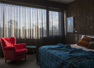 A modern bedroom featuring a red armchair, a bed with a blue and green quilt, and brown and gold textured walls.