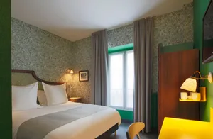 A serene modern bedroom with a white bed, green floral wallpaper, and natural light streaming through the window.