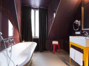 A modern bathroom with a white bathtub, brown tiles, and red stool.