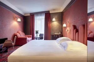 Modern hotel room with a bed, armchair, sofa, and coffee table.