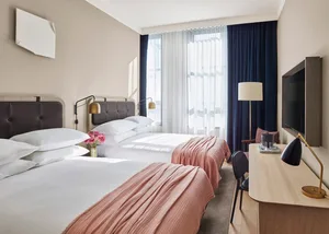 A modern bedroom with soft pink textiles and wooden furniture, featuring minimalistic design elements and natural light.