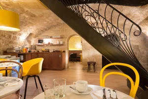 Modern cafe interior with wooden stairs, yellow chairs, and a rustic stone wall