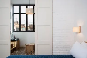 A minimalist bedroom featuring a white brick wall and a bed with a blue and white bedspread.