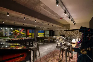 A spacious game room featuring a large table with colorful decorations and various gaming machines, including an arcade cabin