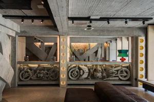 A modern, industrial-style living room featuring exposed concrete walls and ceiling, with a motorcycle centerpiece and a mix 