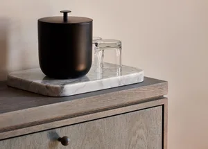 A modern marble side table with a black container and two transparent glasses.