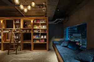 A minimalist library interior featuring concrete and wooden surfaces, with a ladder leading to elevated bookshelves.