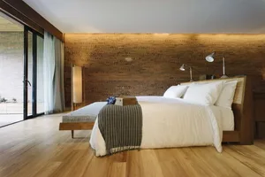 A modern minimalist bedroom with wood flooring, white bedding, and a wooden headboard.