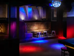 A modern nightclub interior with plush seating, colorful lighting, and a stage area.