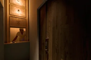 A wooden reception desk with a glass top and a man standing behind it in the dark.