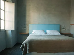 A minimalist bedroom featuring a textile-covered blue headboard and neatly made bed.