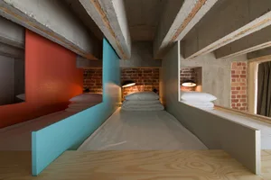 A minimalist bedroom with floating beds and exposed concrete beams, featuring brick walls and white linens.