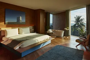 A minimalistic bedroom featuring a large bed with a blue and white blanket, next to a bathtub and a large window with a view