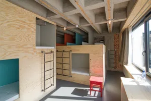 A minimalist industrial bunk bed with wood paneling and a red stool in a residential setting.