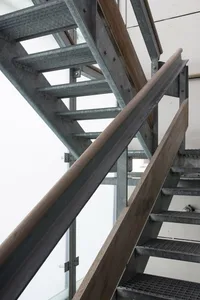 Metallic stairs leading upwards with wood railing and handrail.