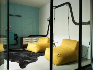 A minimalist living room with yellow fabric and leather chairs, white walls, and glass walls, featuring a cowhide rug.