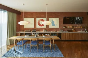 Modern dining room with wooden furniture, including a long table, blue chairs, and a blue rug.