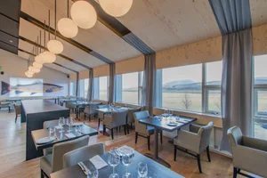 Industrial-style restaurant interior with wooden furnishings and large windows providing natural light.