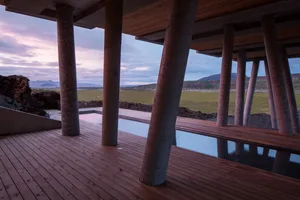 An outdoor modern spa with a concrete hot tub surrounded by wooden decks, set against a scenic landscape with mountains and a